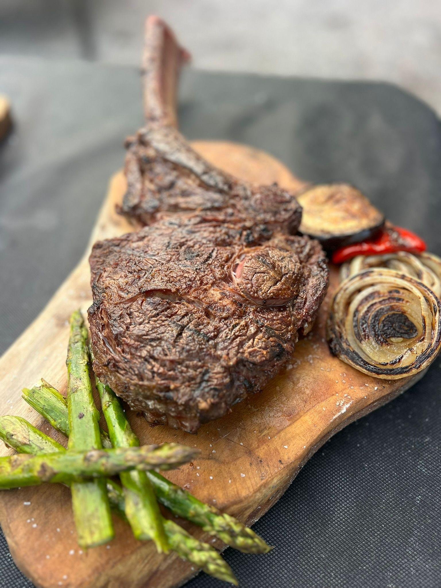 Chuletón a la parrilla recién cortado, con espárragos y cebolla asada